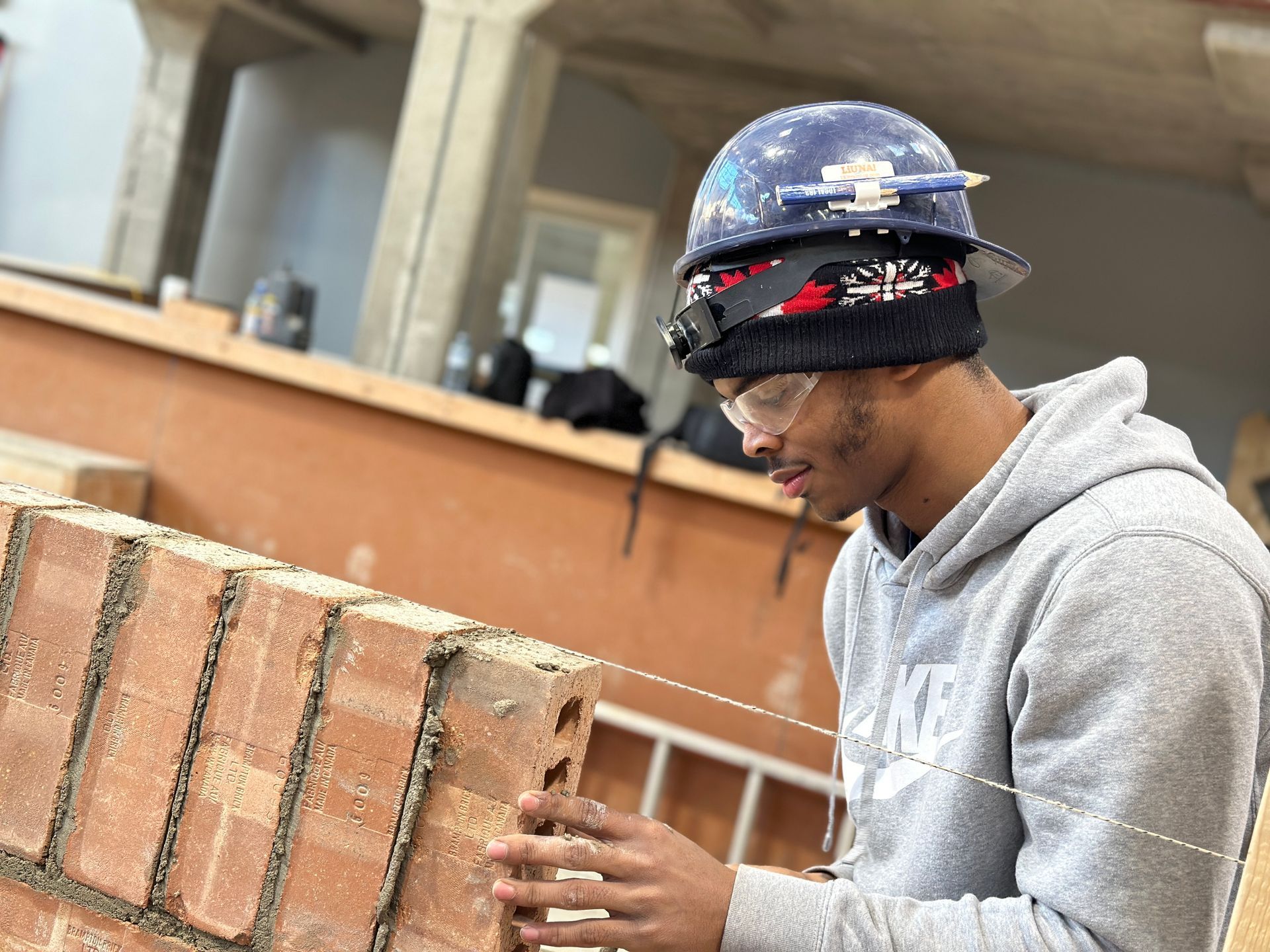 A man wearing a hard hat and safety glasses is working on a brick wall.