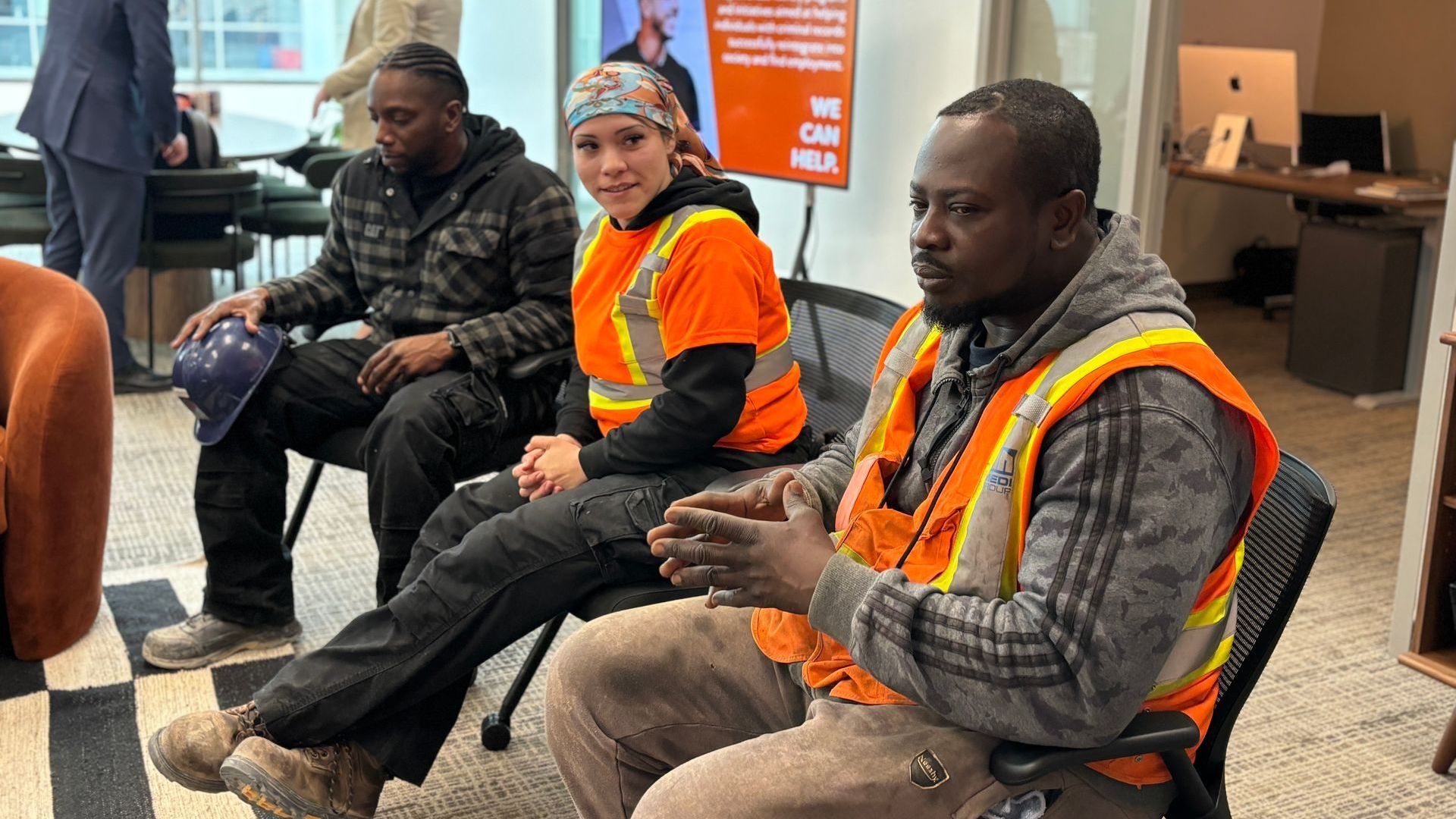 A group of construction workers are sitting talking in a room.