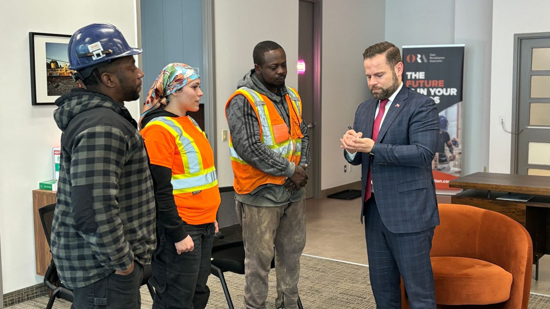 A man in a suit and tie is talking to a group of construction workers.