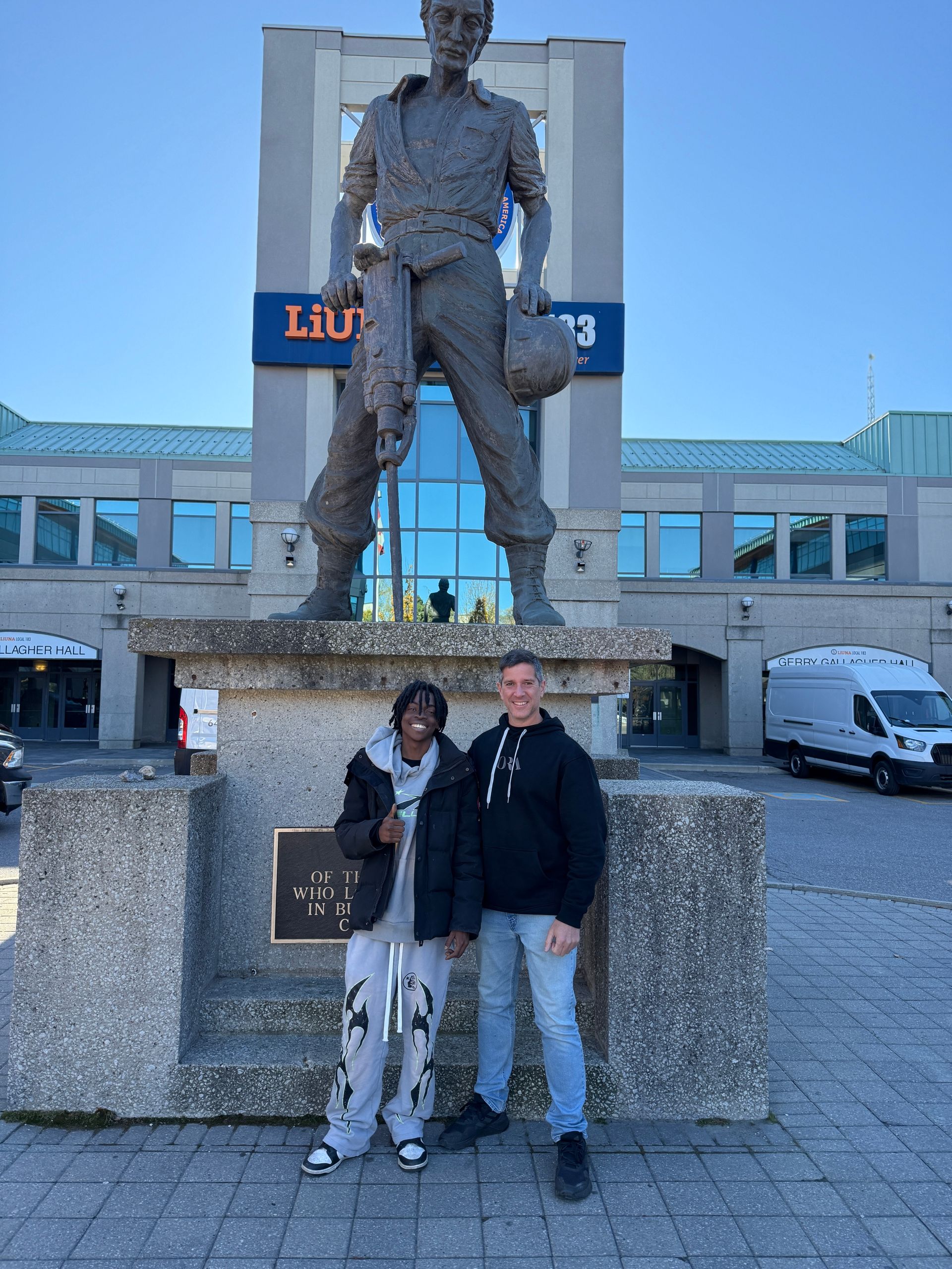 Two people standing in front of a statue of a man with a helmet