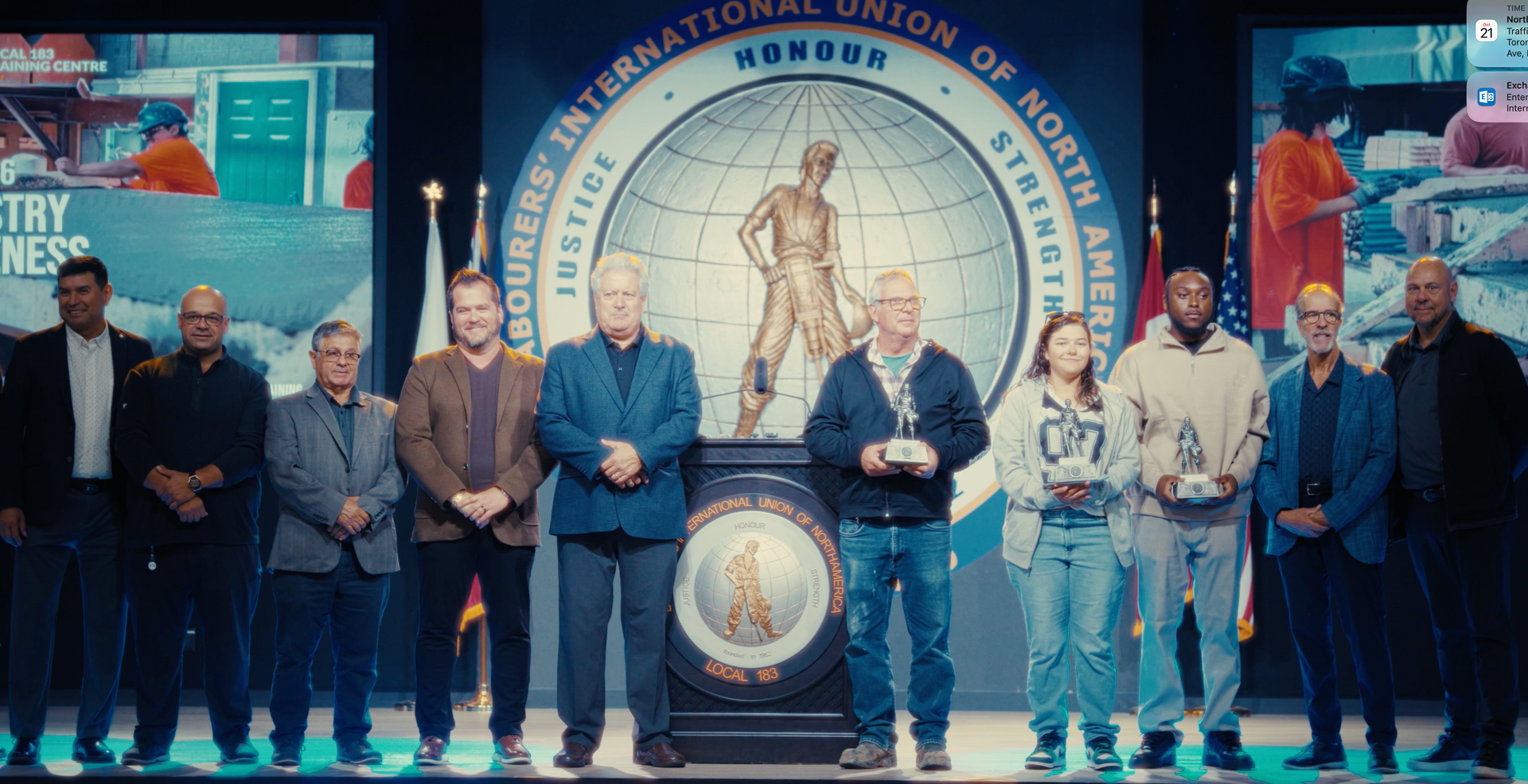 Panel of officials standing onstage at a podium before a large circular event backdrop.