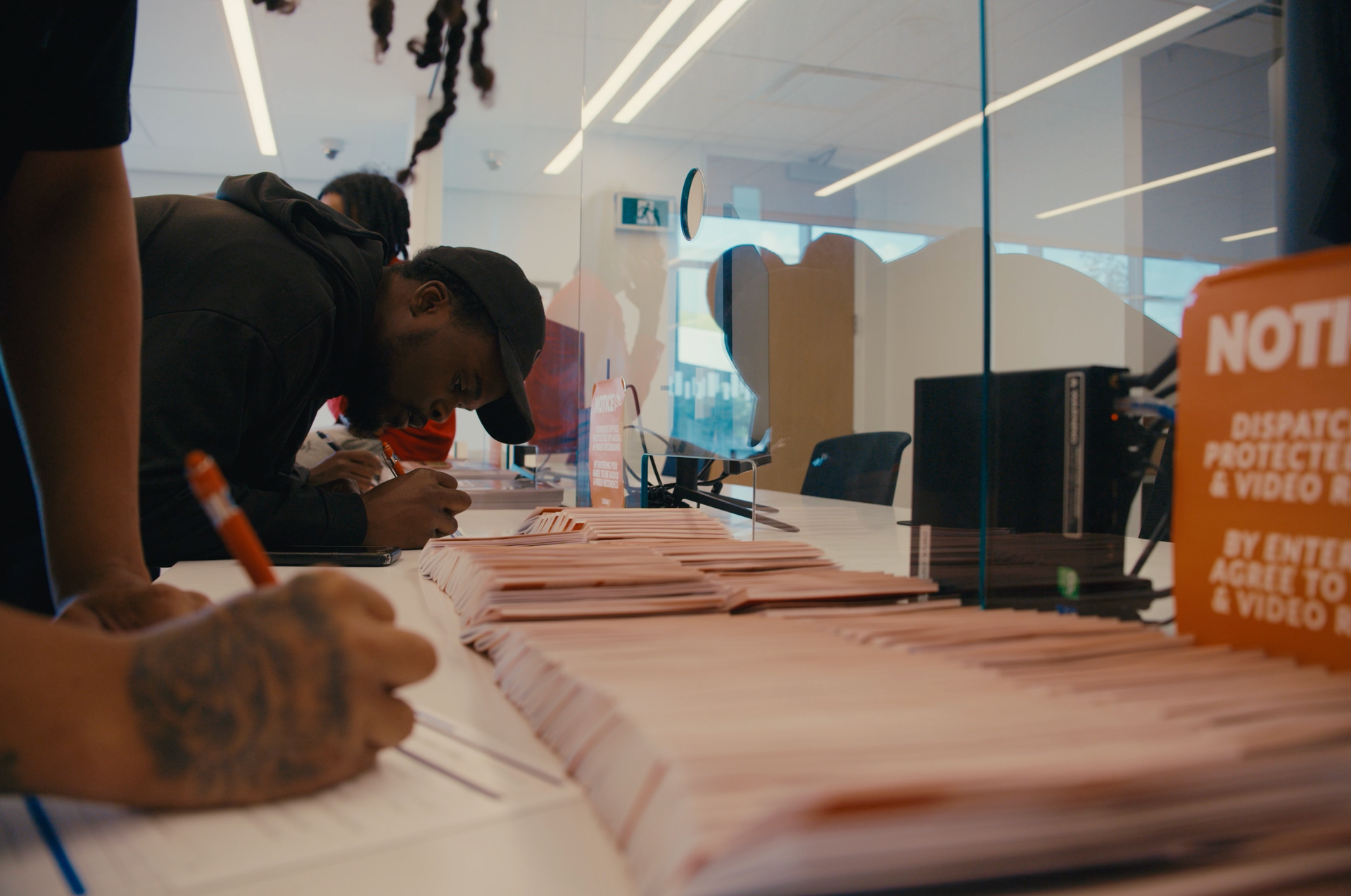 People signing papers at a registration table in a glass-walled office lobby