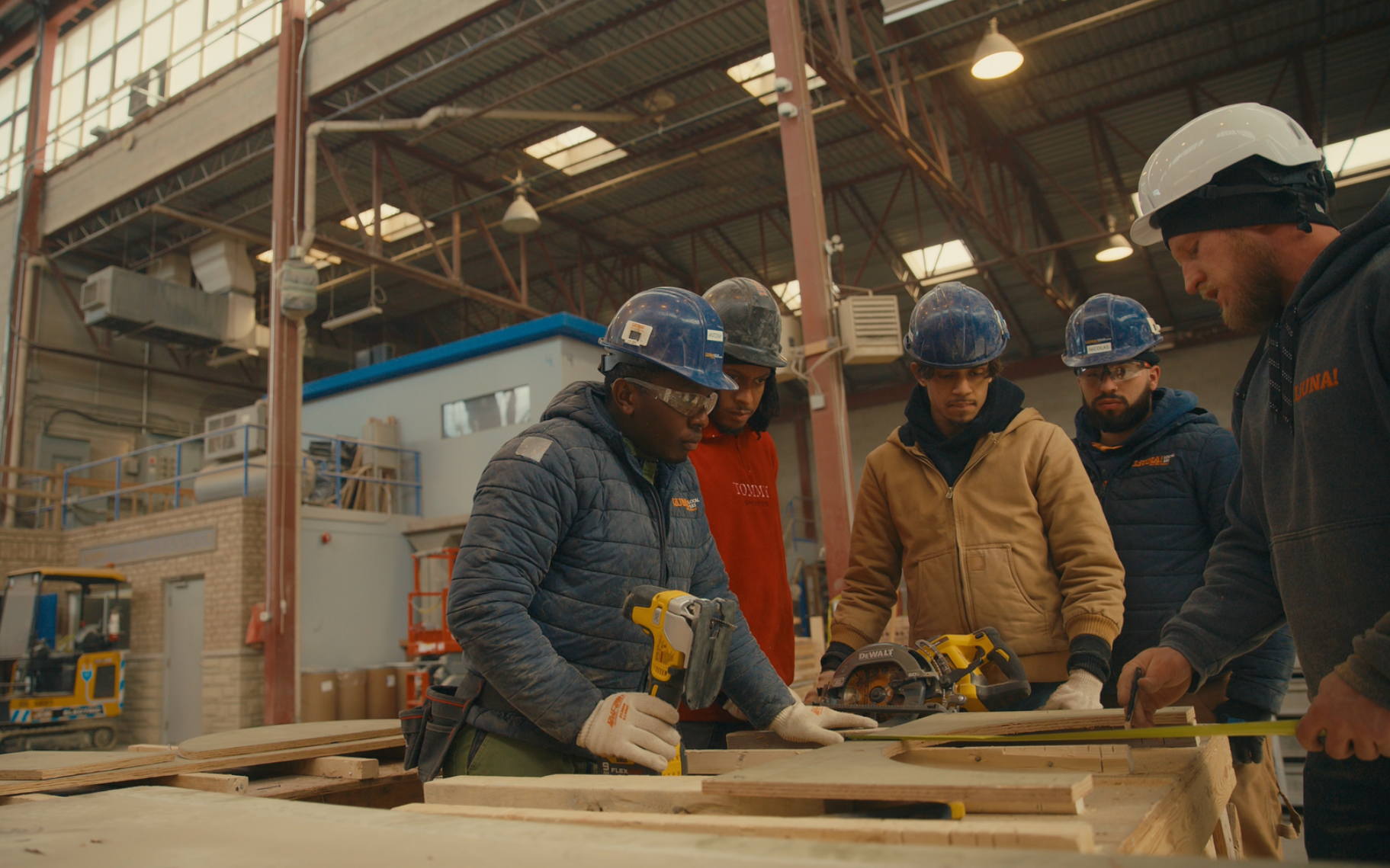Workers in hard hats examining wood planks at a factory workbench