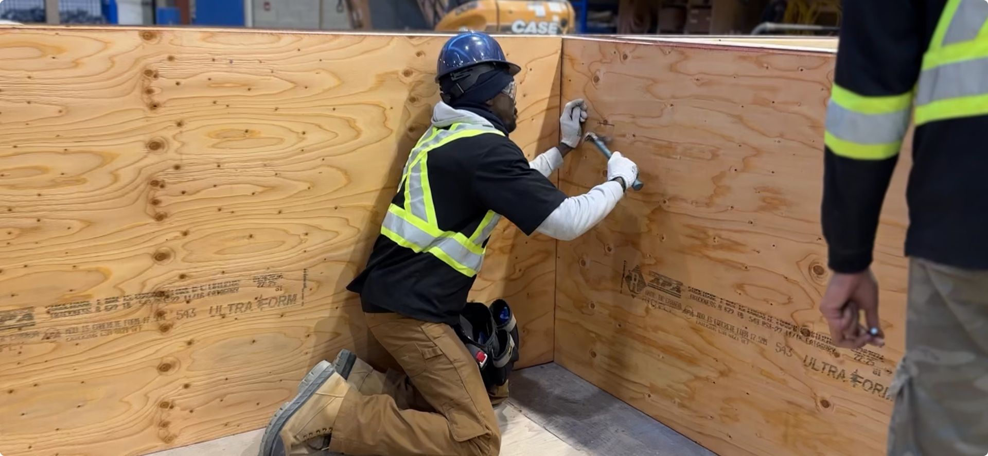 A man is kneeling down in front of a wooden wall holding a hammer. A man is kneeling down in front of a wooden wall holding a hammer.