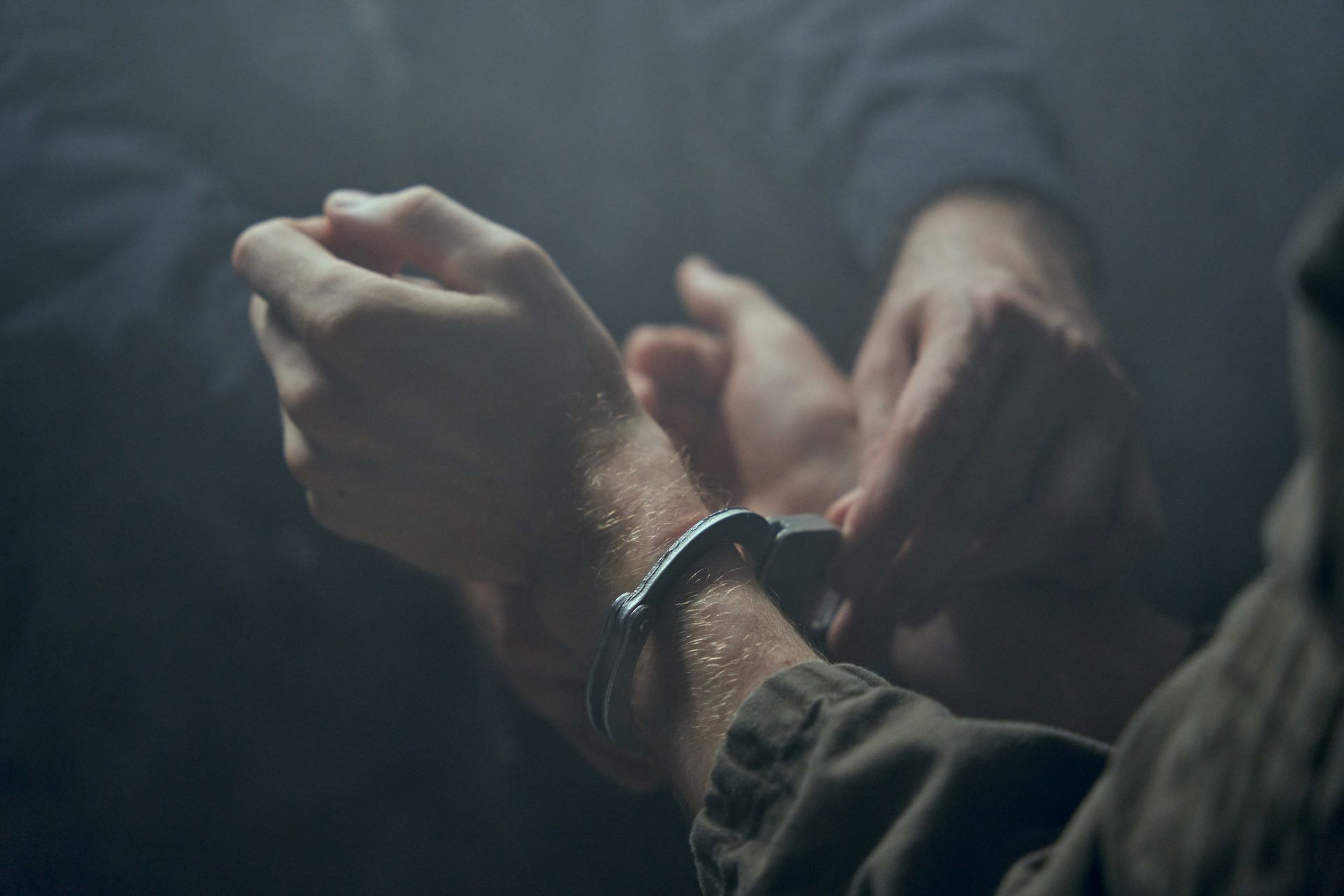 Hands restraining another person’s wrist in a dark, tense close-up scene