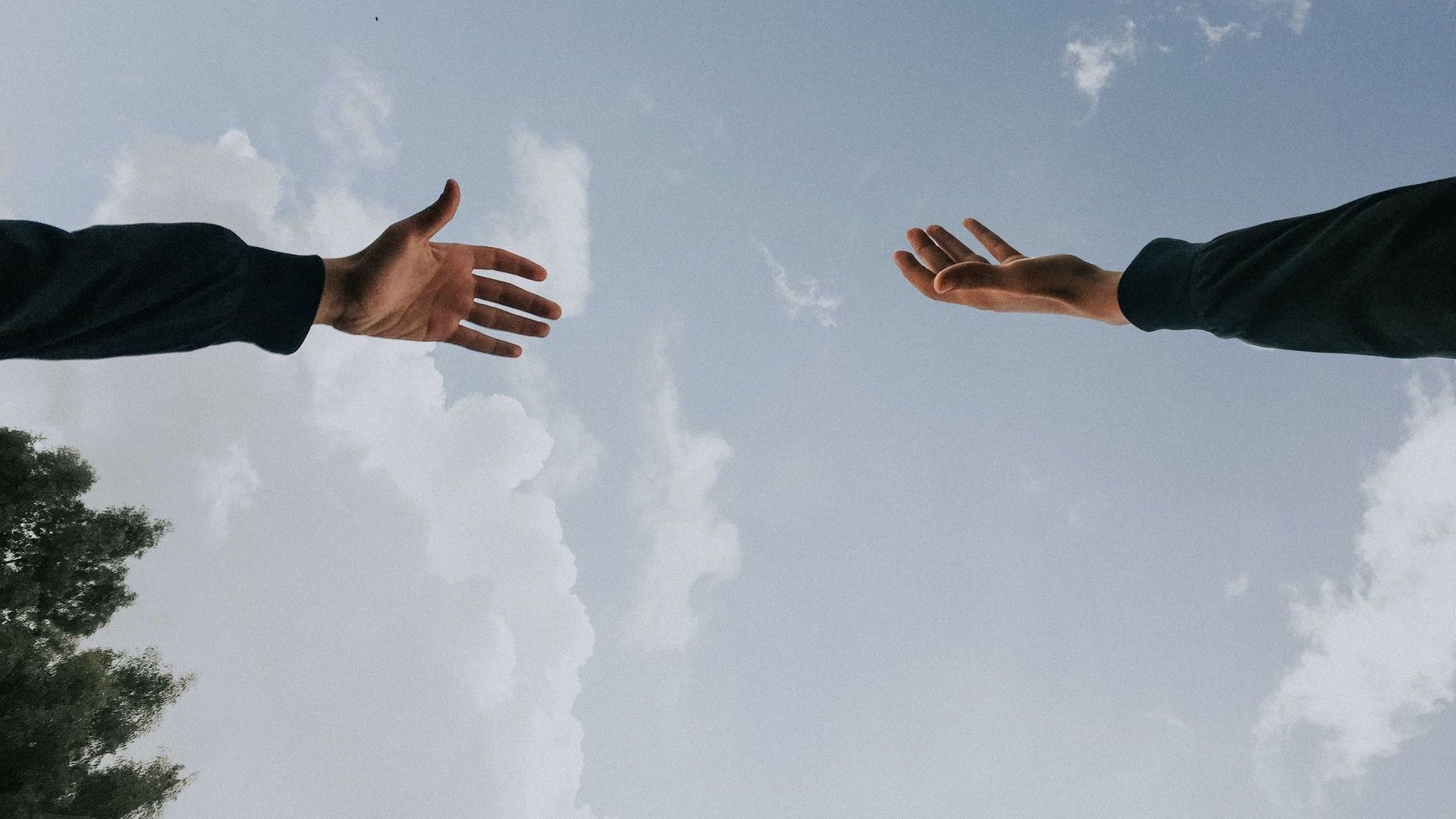 Two outstretched hands reaching toward each other against a cloudy sky