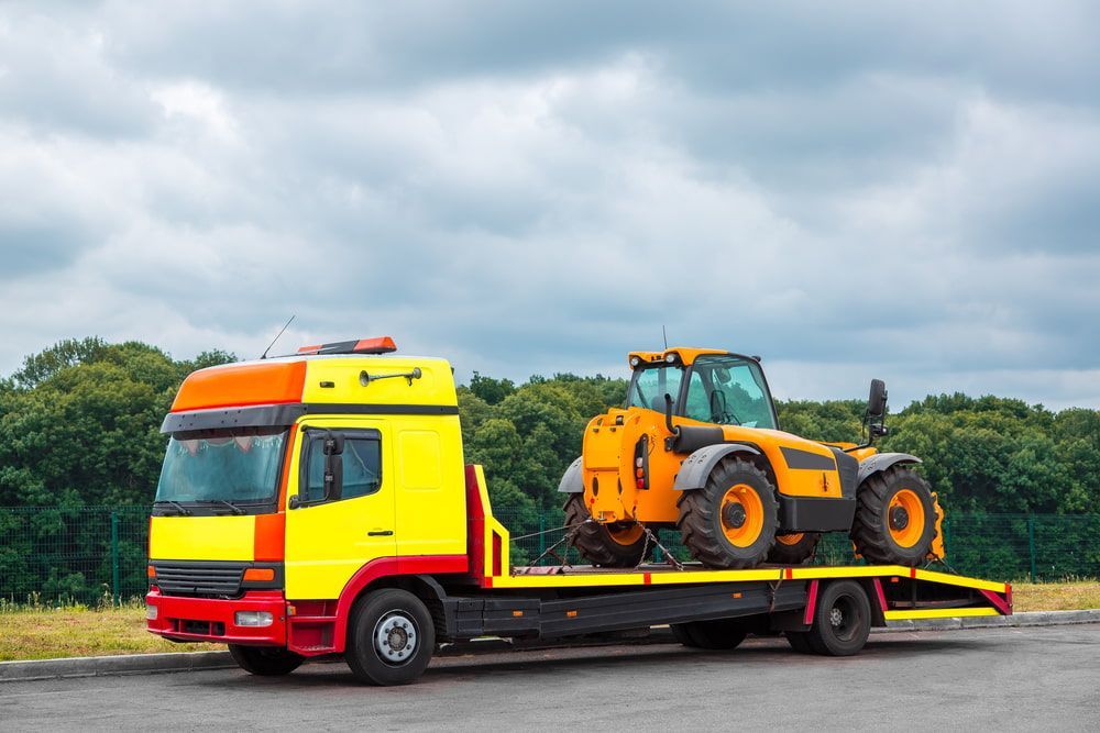 A Tow Truck is Carrying a Yellow Tractor on the Back of It — Mareeba Express Towing in Cairns, QLD
