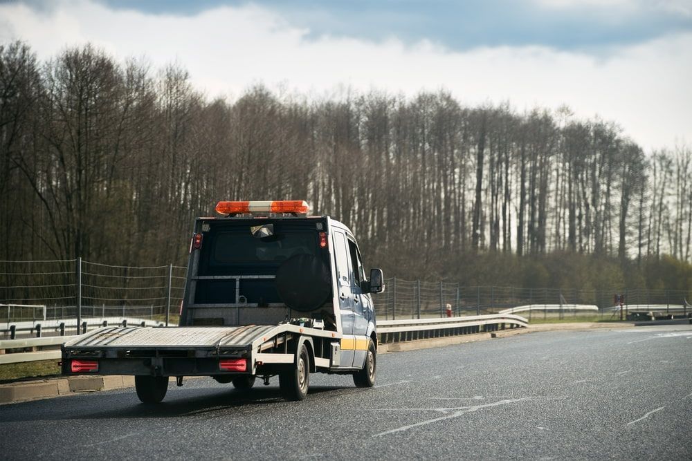 A Tow Truck is Driving Down a Highway Next to a Forest — Mareeba Express Towing in Townsville, QLD