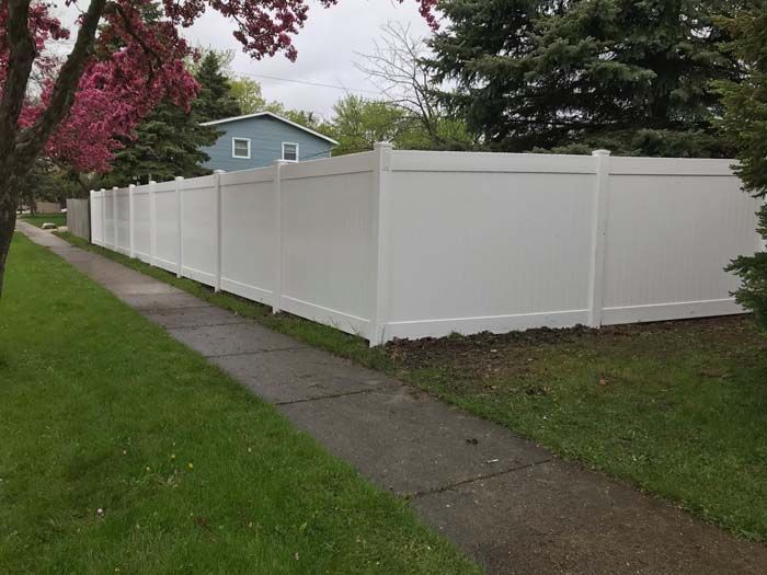A white fence along a sidewalk next to a house.