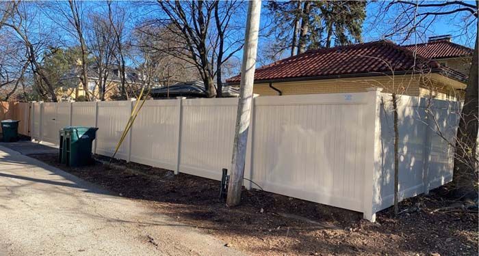A white fence is surrounding a house on the side of a road.