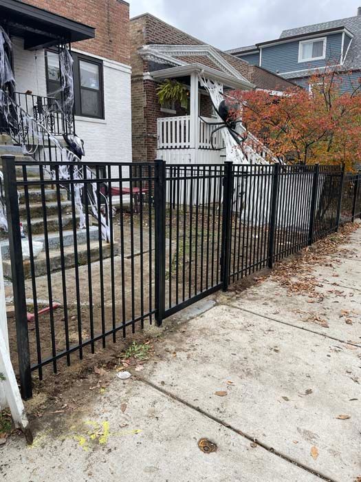 A black metal fence is surrounding a house on a sidewalk.