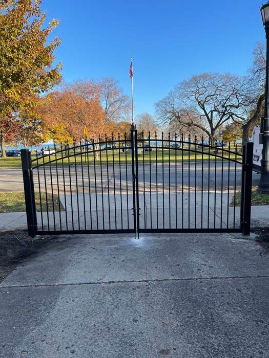 A black wrought iron gate is sitting on a sidewalk in front of a park.