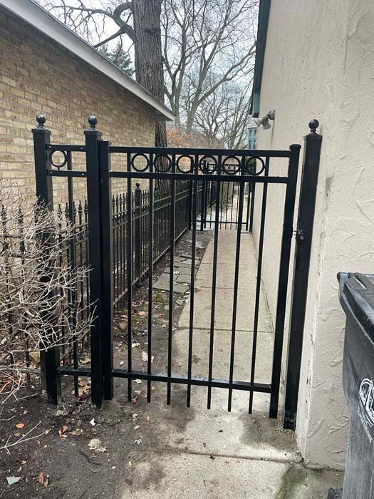 A black wrought iron gate leading to a sidewalk next to a brick building.