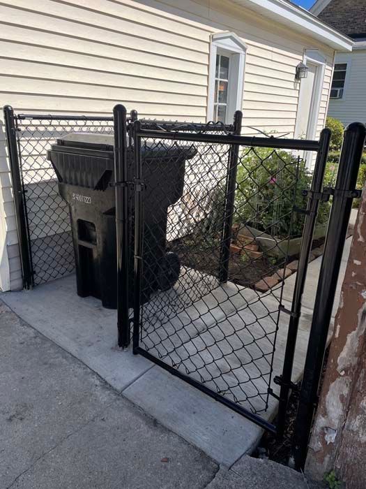 A black garbage can is behind a chain link fence