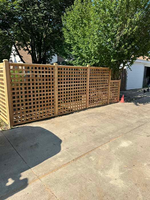 A wooden fence is sitting on the side of a driveway next to a garage.