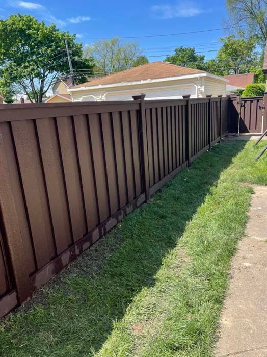 A brown fence surrounds a lush green yard next to a sidewalk.