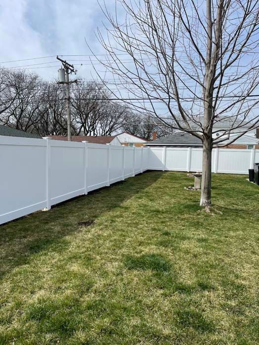 A white vinyl fence surrounds a lush green yard.