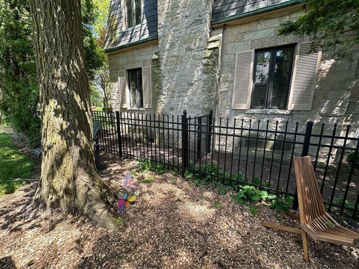 A wooden chair is sitting in front of a stone building next to a fence.