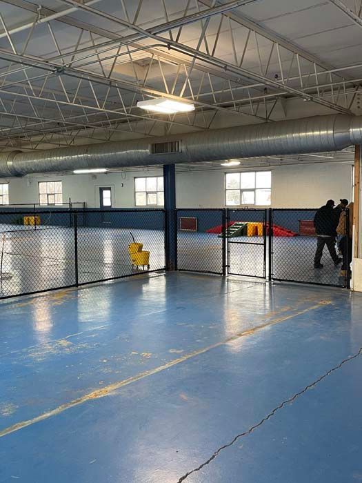 A large empty warehouse with a blue floor and a fence.