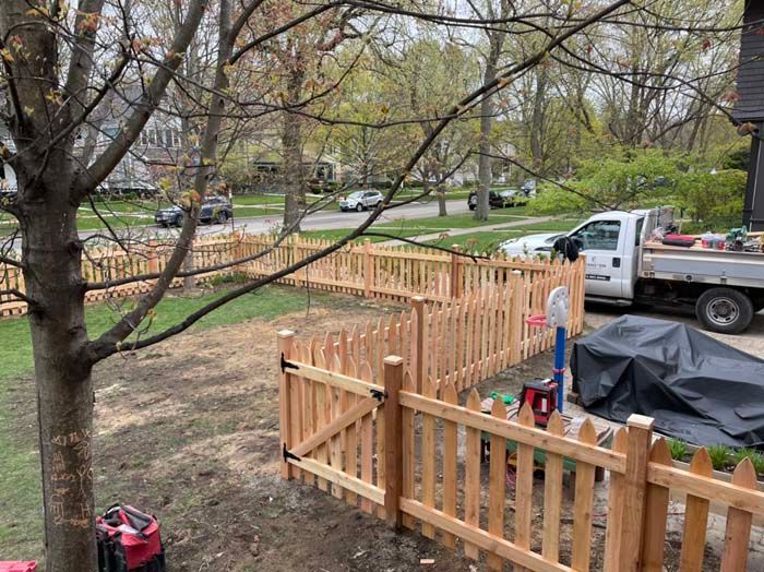 A wooden picket fence is being built in a backyard.