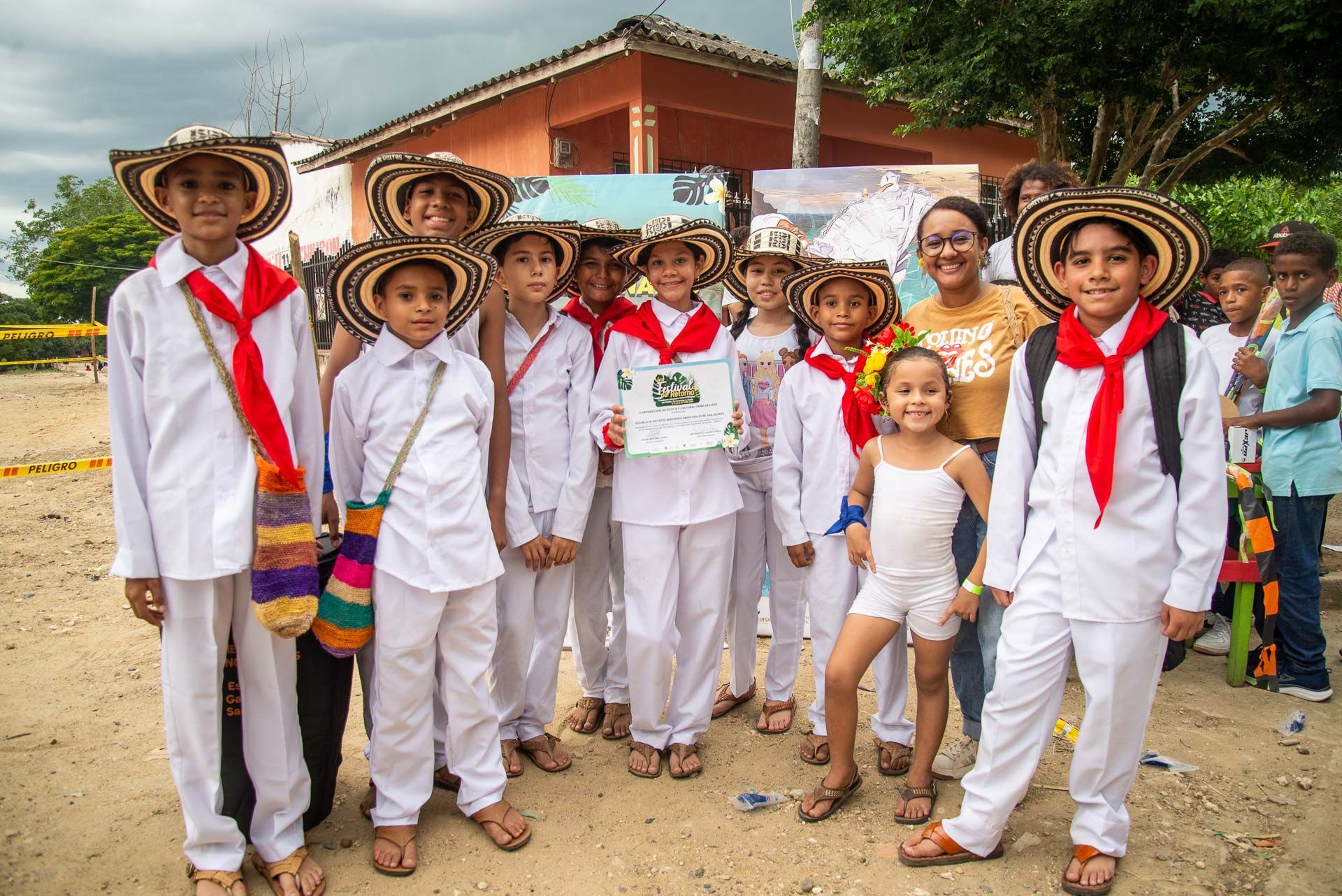 Grupo de niños con trajes blancos y sombreros sonriendo, con una mujer, al aire libre.