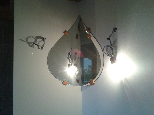 Specchio a forma di lacrima nell'angolo, che riflette la luce. Occhiali e applique nelle vicinanze.