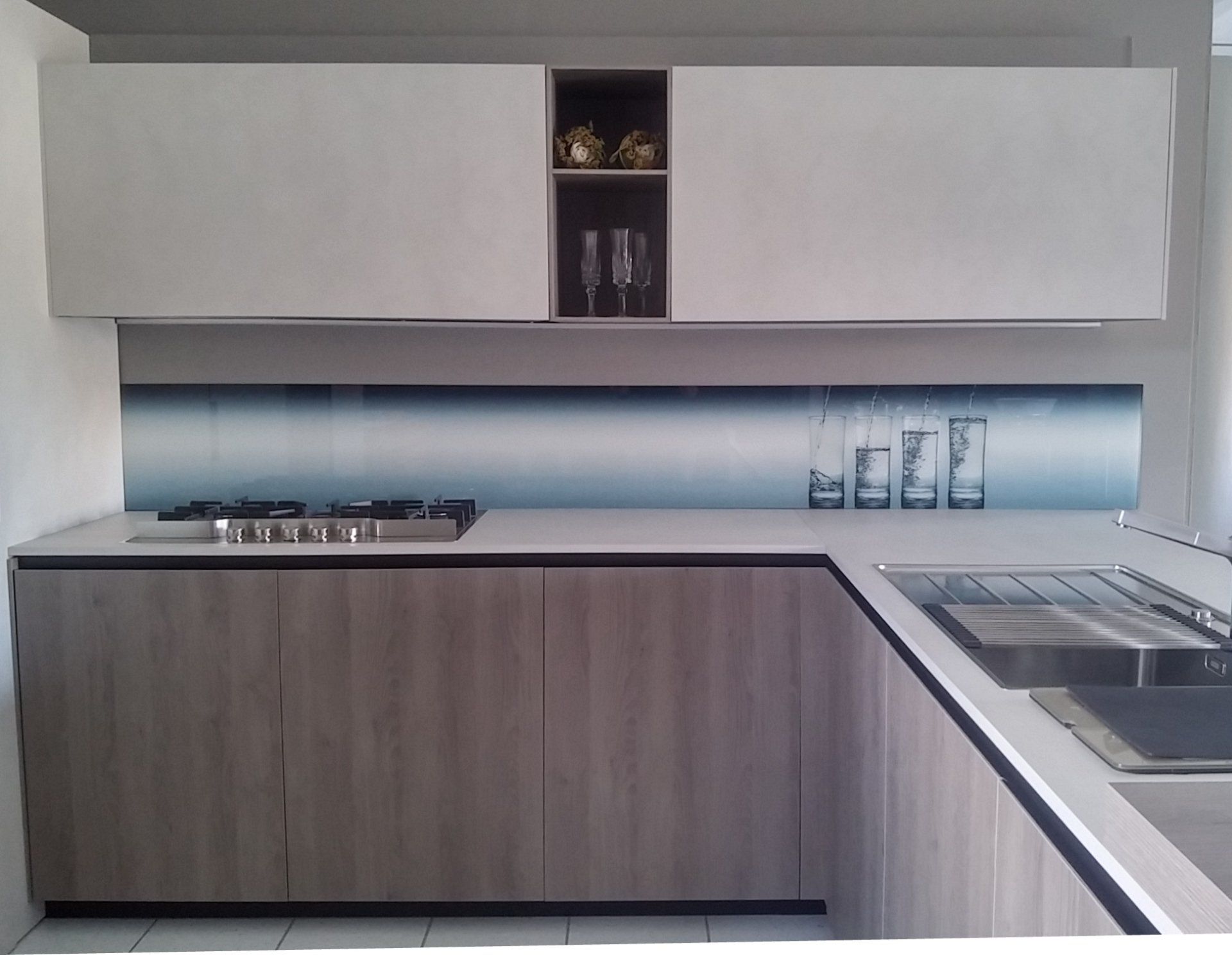 Cucina moderna con mobili in legno chiaro, ripiani bianchi e paraschizzi blu.