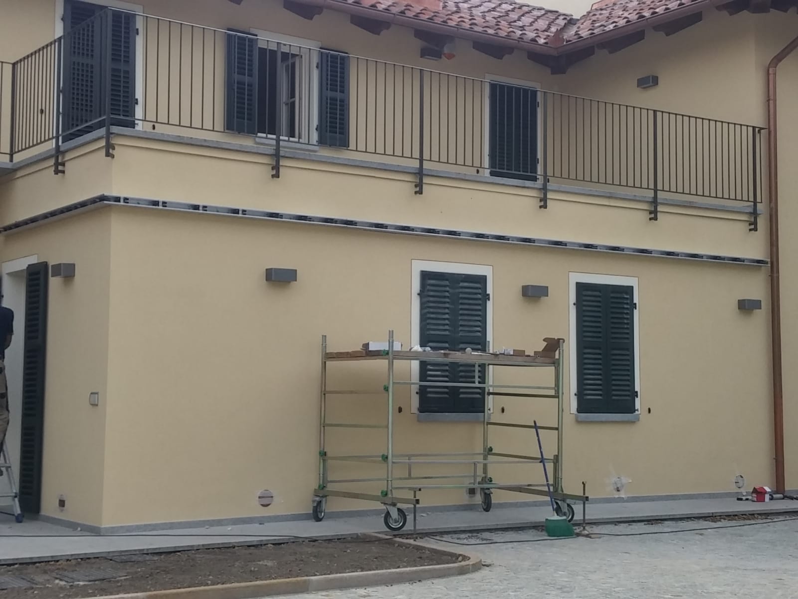 Edificio giallo con persiane nere e ringhiera del balcone; impalcature di fronte.