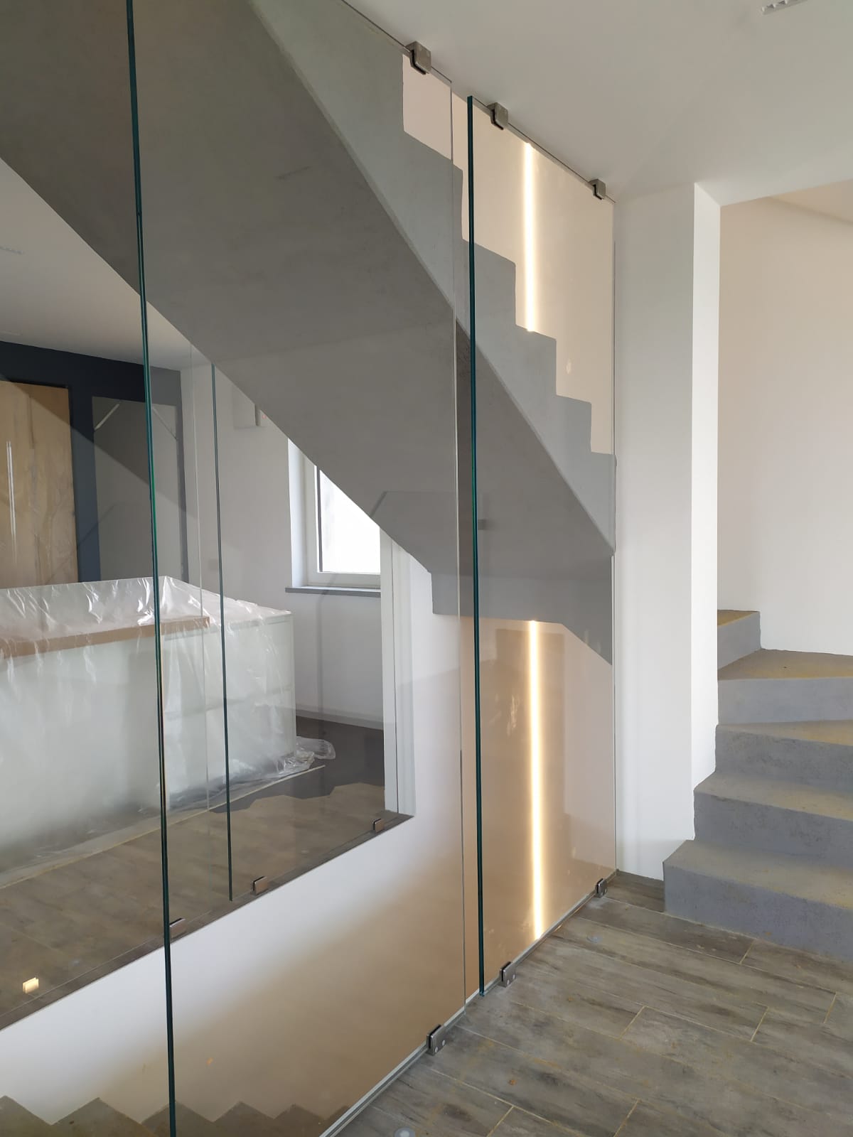 Scala moderna con ringhiera in vetro. Gradini grigi, pareti bianche e pavimento effetto legno.