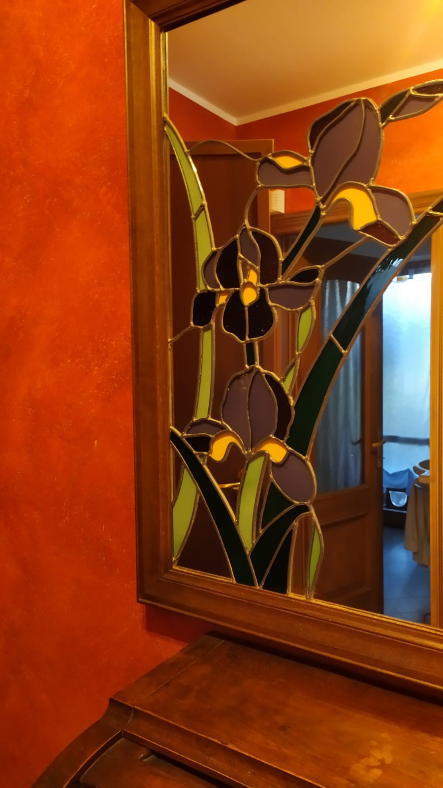 Specchio con fiori di iris in vetro colorato; cornice in legno su parete arancione.