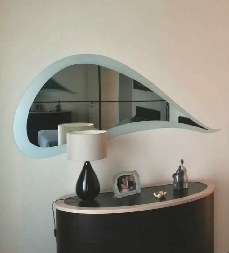 Specchio ovale sopra una consolle bianca e nera con lampada e decorazioni su una parete bianca.