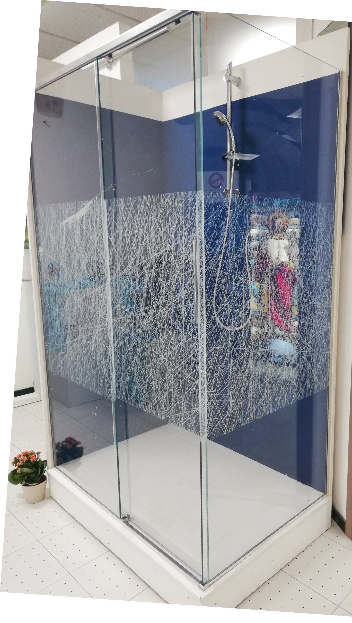 Box doccia con porte in vetro, parete decorata con motivi blu e bianchi e soffione.