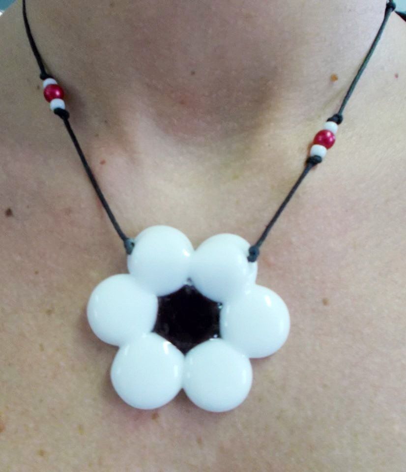 Collana con ciondolo a forma di margherita bianca, cordino nero e perline rosse/bianche.