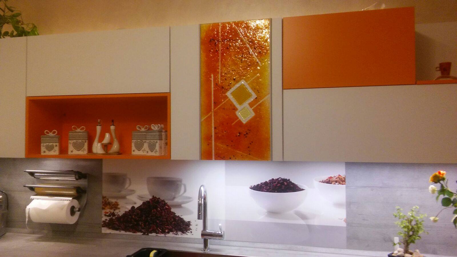 Cucina con mobili bianchi, dettagli arancioni e un pannello decorativo in vetro.