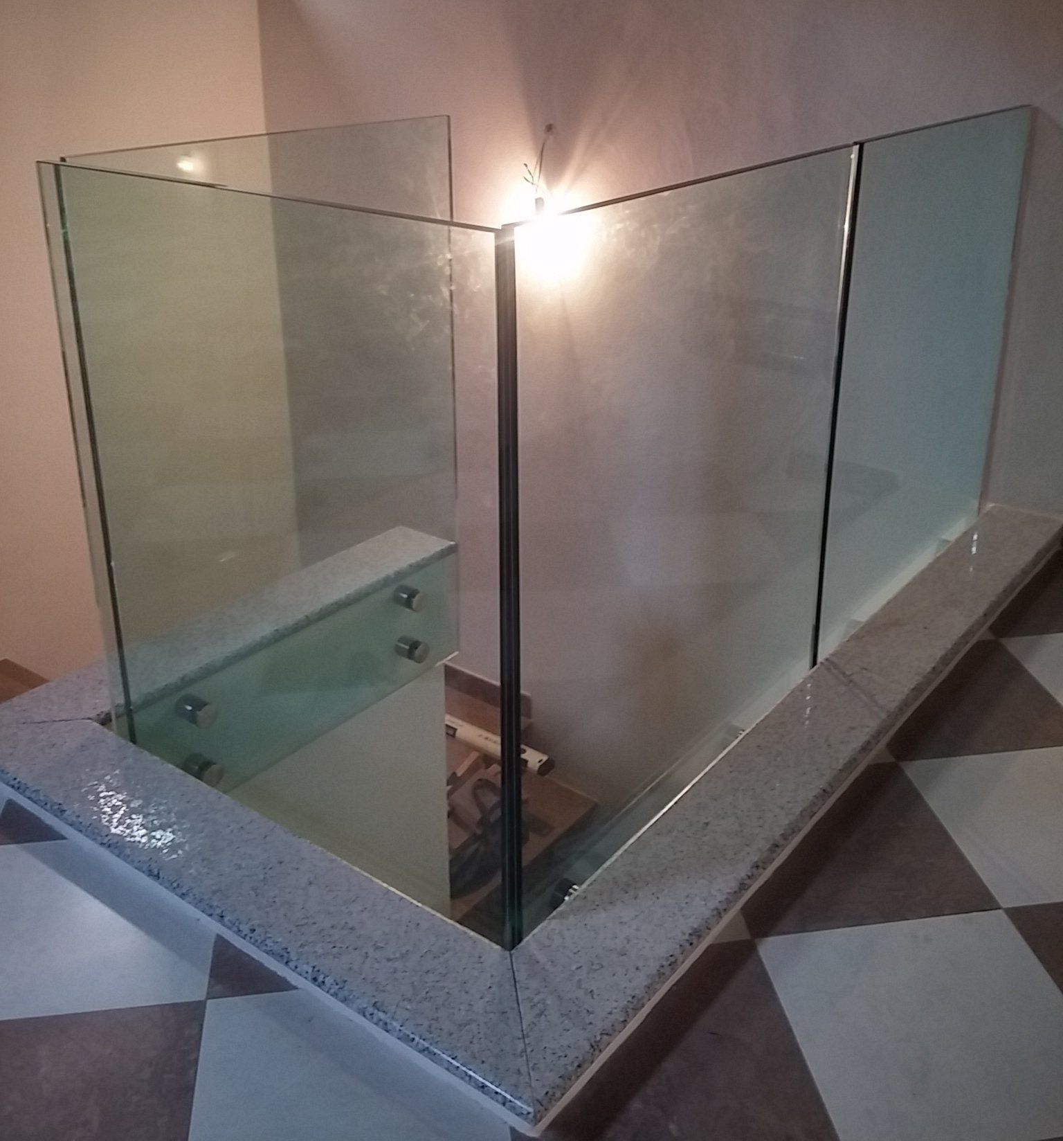 Ringhiera in vetro che circonda il pianerottolo della scala. Base in piastrelle chiare con pannelli in vetro trasparente.