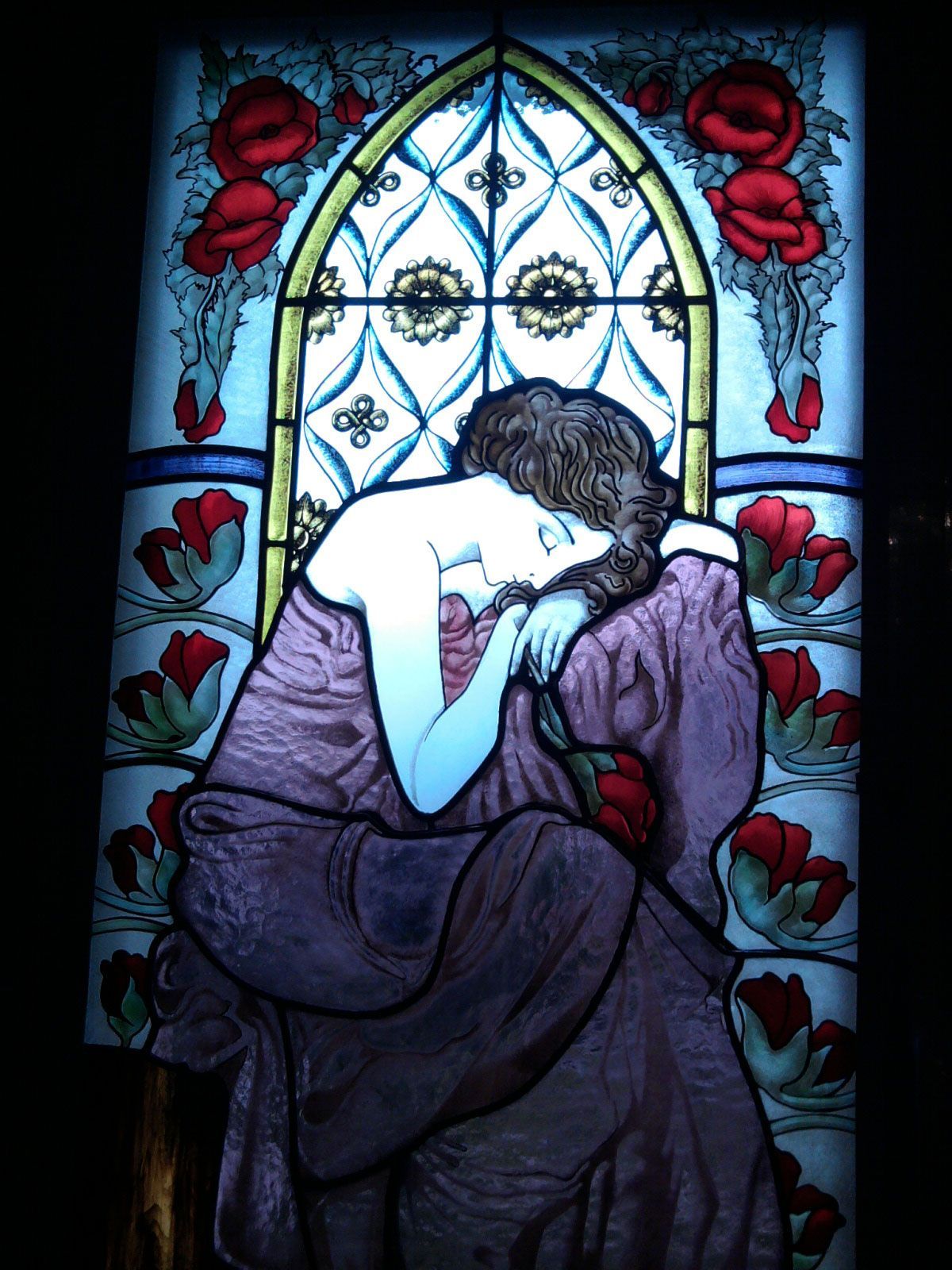 Vetrata: donna in viola, testa appoggiata, fiori rossi, finestra ad arco con sfondo decorato.
