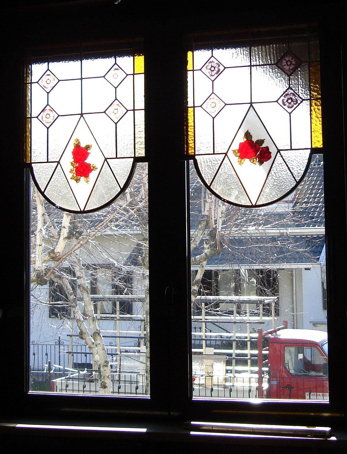 Vetrata con rose rosse e motivi geometrici; vista di un paesaggio innevato all'aperto.