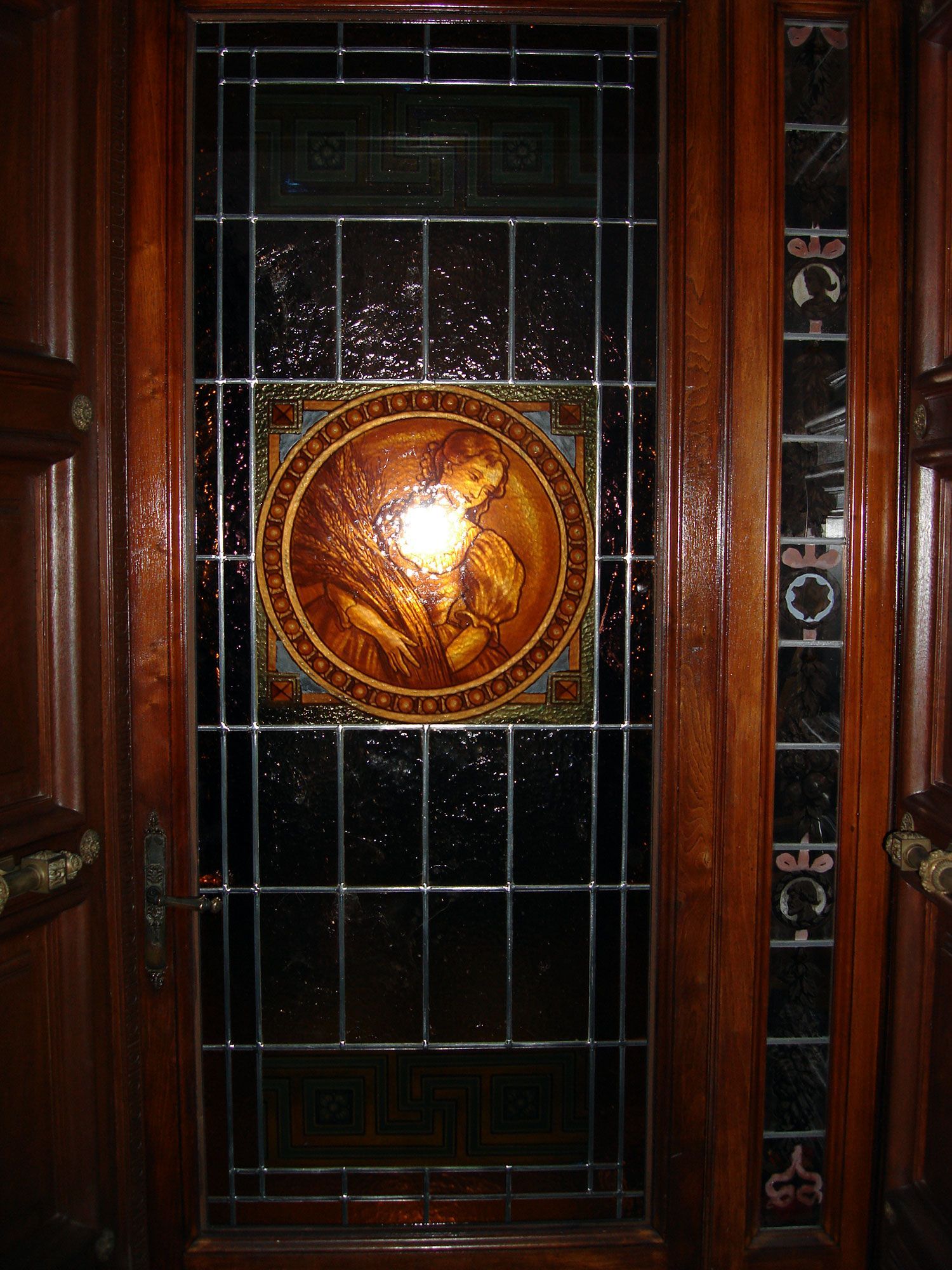 Porta in legno con pannello in vetro colorato raffigurante un'immagine rotonda di una persona che raccoglie il grano.