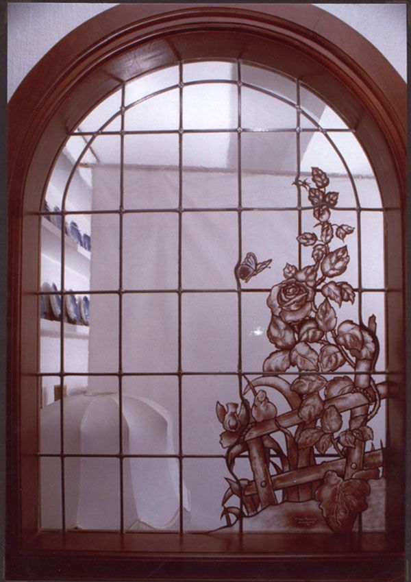 Vetrata con motivo di rose e farfalle; inserita in una cornice ad arco in legno.