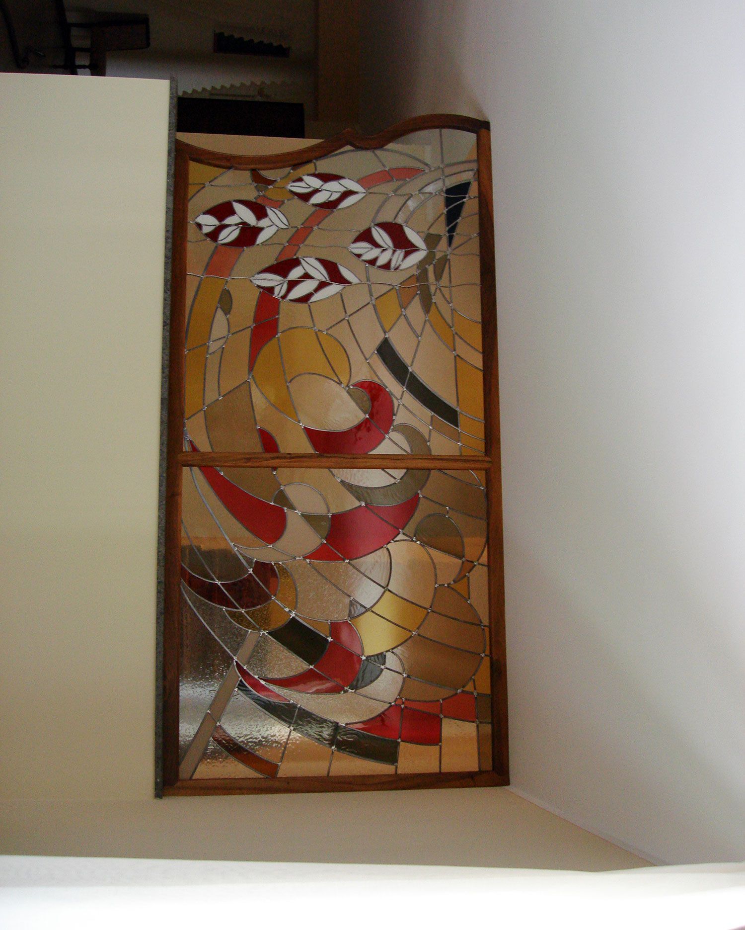 Pannello di vetro colorato con forme astratte in rosso, oro e marrone, incorniciato in legno. Montato a parete.