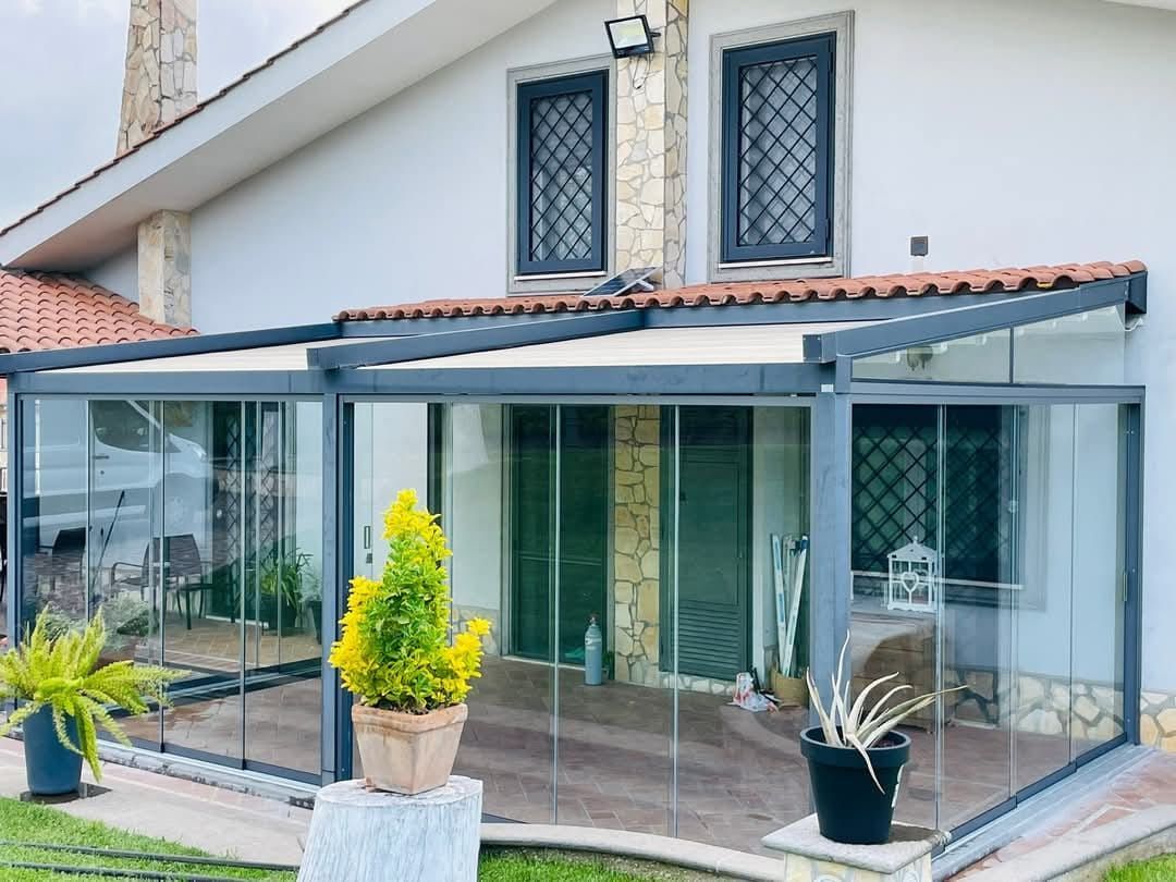 Estensione del patio in vetro di una casa con tetto coperto, piante e finestre.