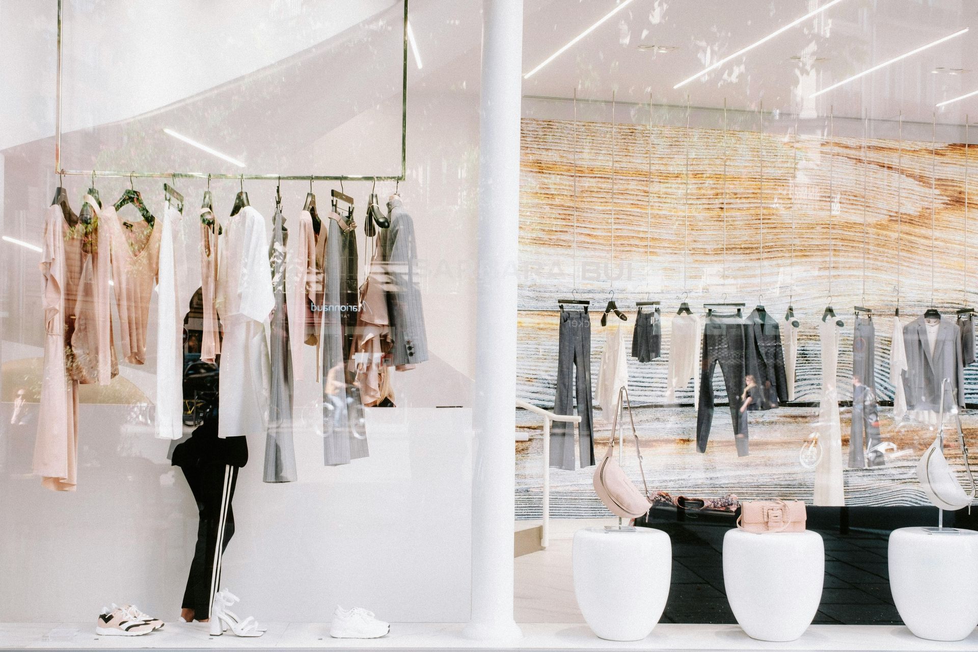 Minimalist clothing boutique with pastel garments on racks and white stools in a bright, airy interior