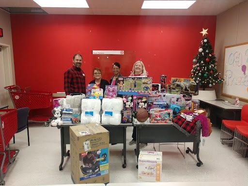 Group of people with donated toys and Christmas tree. Red wall, Target logo visible.