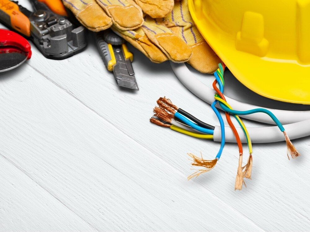 An Electrician Helmet, Gloves, Pliers, Wire and Other Tools on a Wooden Table — Proserpine Electrical Services in Whitsundays, QLD