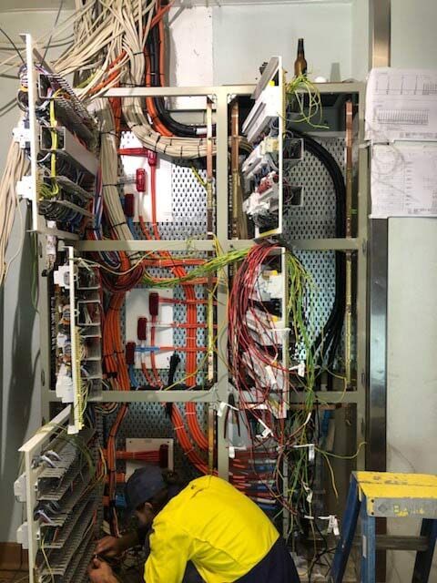 Man in a Yellow Shirt is Working on a Large Electrical Box — Proserpine Electrical Services in Proserpine, QLD
