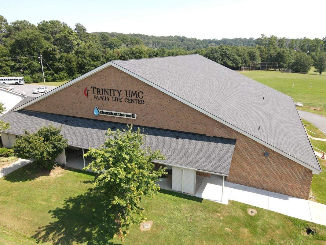 Trinity UMC building, exterior view, brick facade, angled roof, green lawn, trees in background.