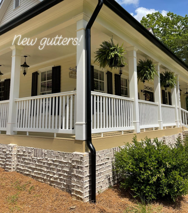White porch with black gutters and hanging plants.
