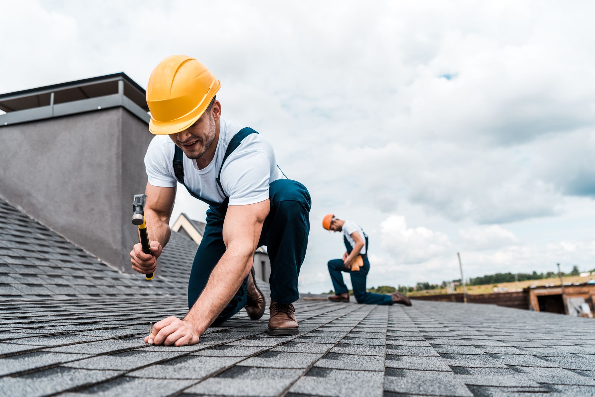 Roofers installing shingles on a rooftop under a cloudy sky.