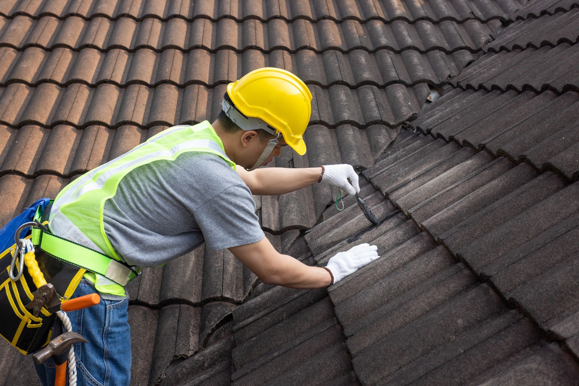 Roofer wearing safety gear repairs tiles on a roof.