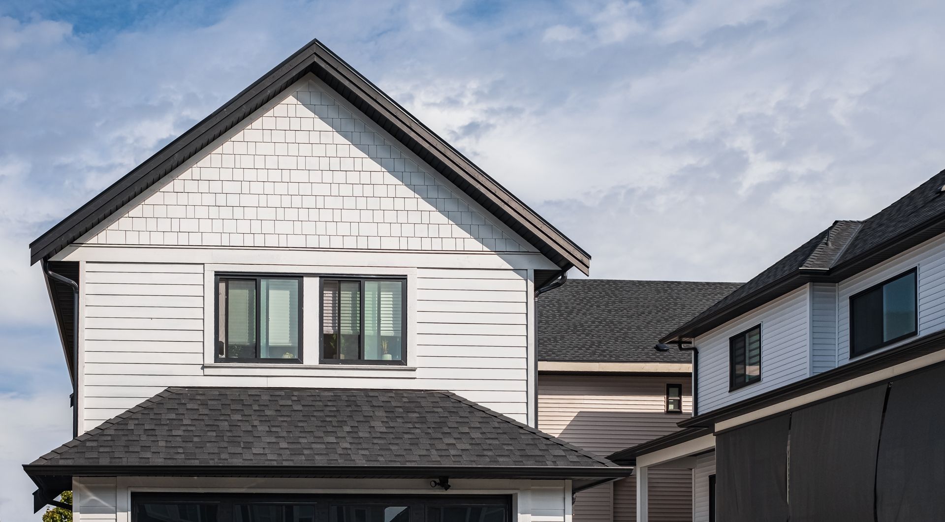 White house with black roof, windows, and garage door against a cloudy sky.